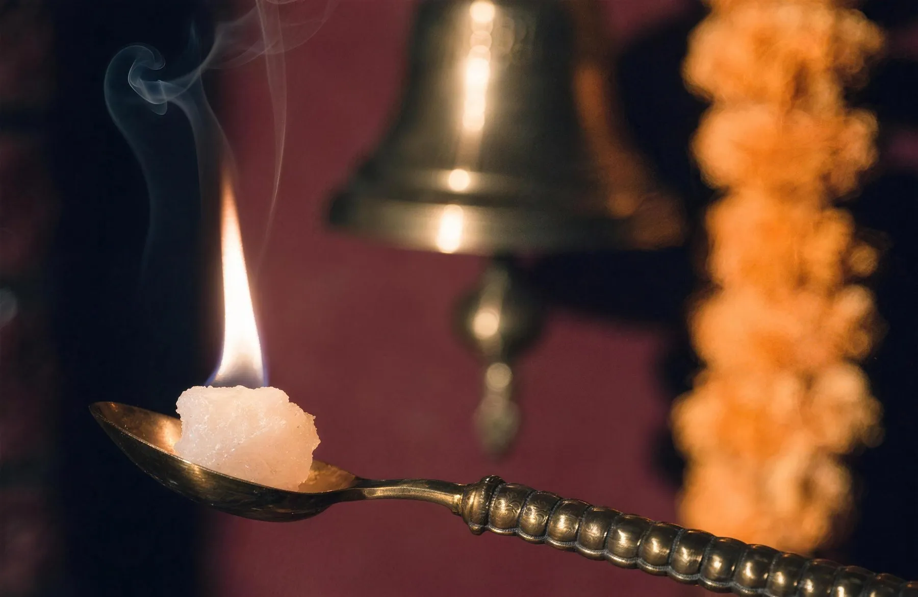Camphor burning with a bright flame on a brass spoon in the dark, a temple bell and marigold garland behind