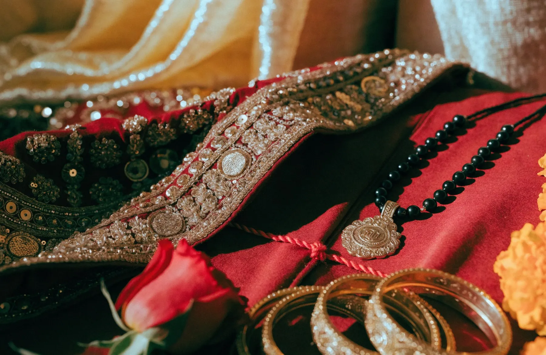 Bridal red and gold embroidery with a mangalsutra, gold bangles, a rose and marigolds resting on it