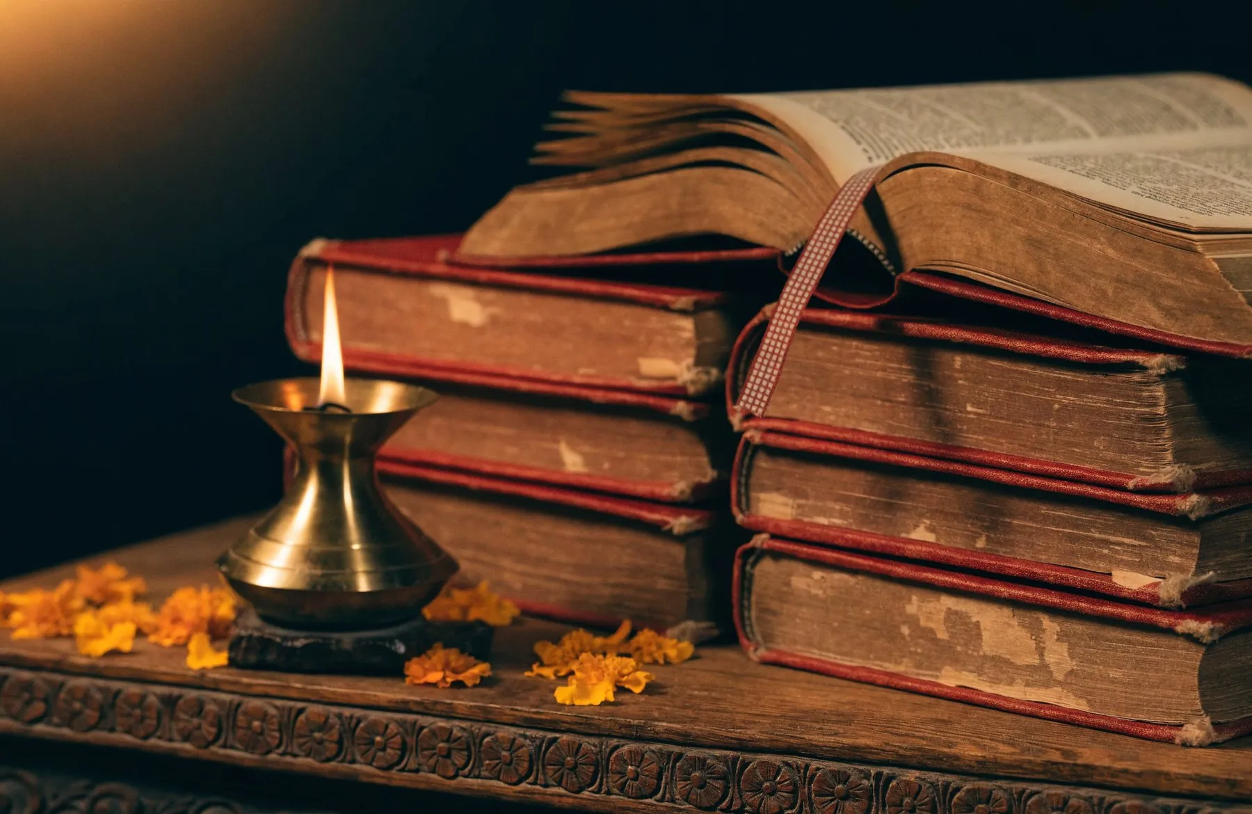 Bound scripture volumes wrapped in red cloth on a carved wooden stand, an oil lamp burning beside them