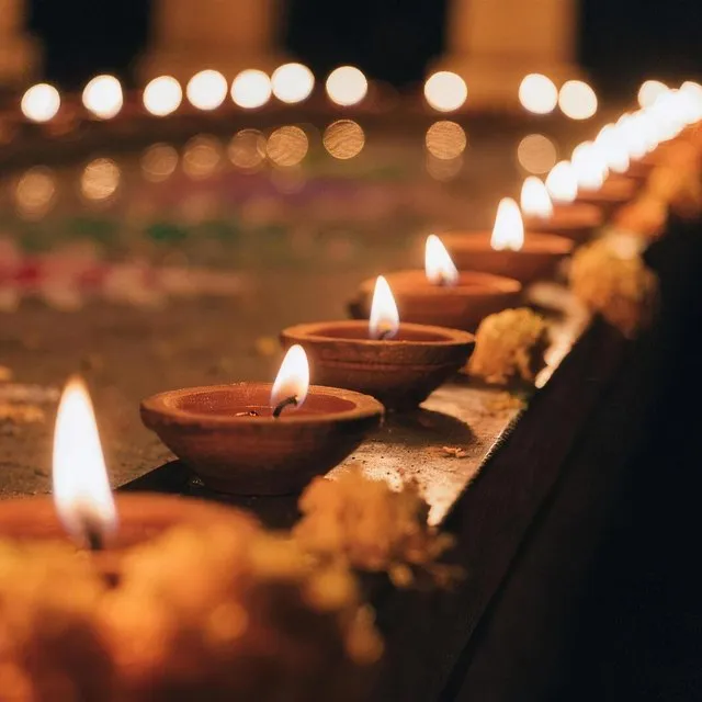 A row of clay diya lamps burning beside marigolds and rangoli