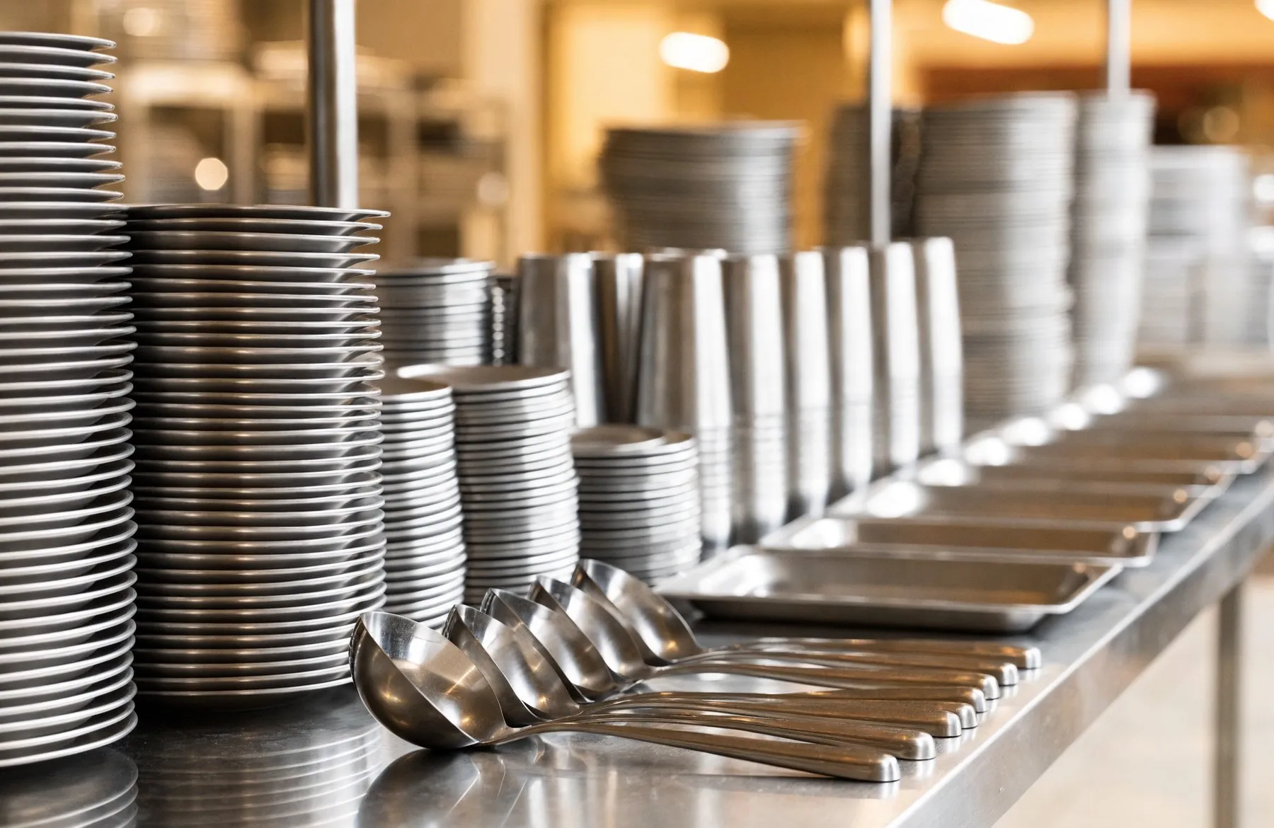 A spotless steel serving counter with stacks of clean plates and tumblers ready for a community meal