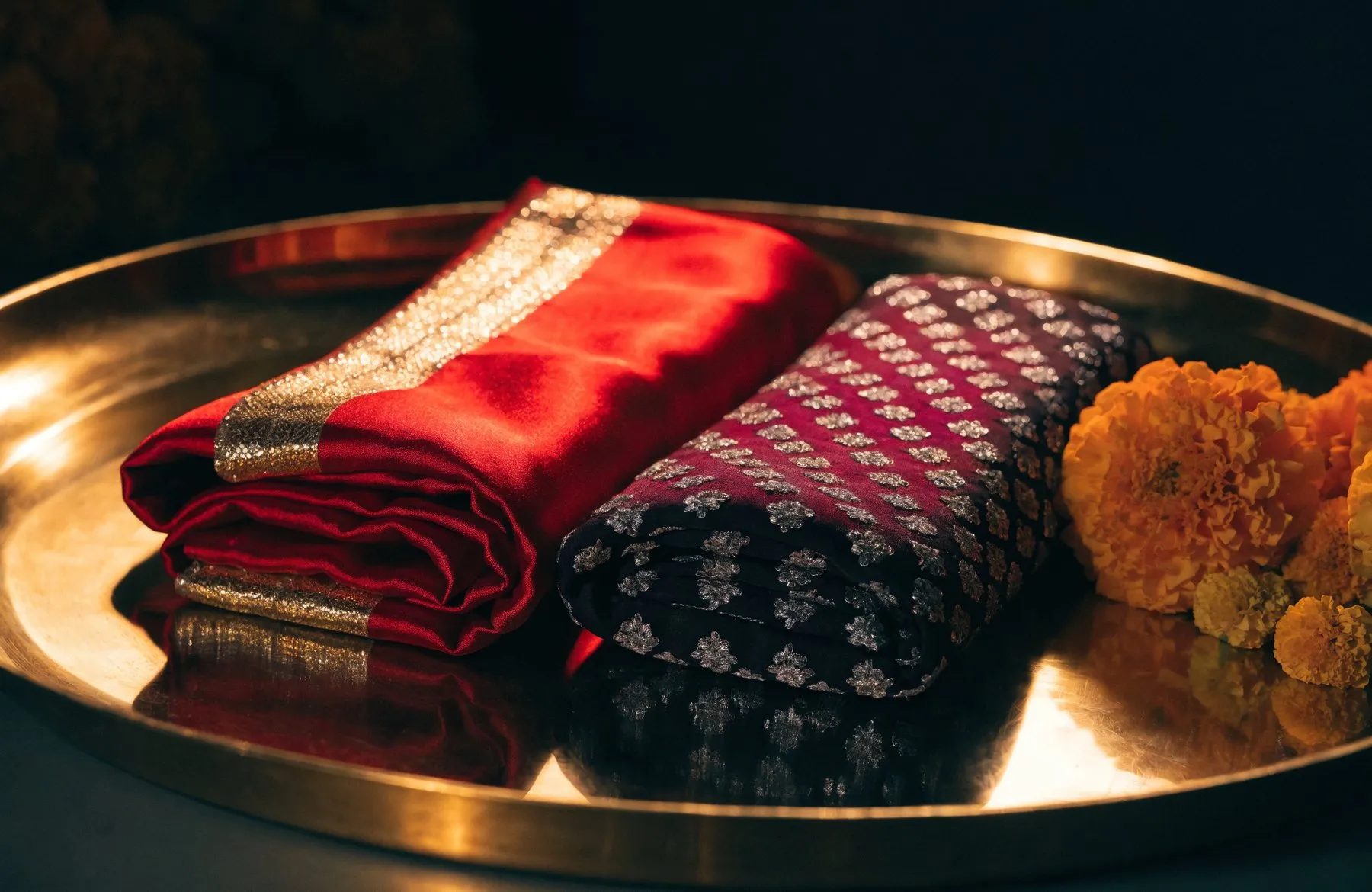 Two folded silk chunris on a brass tray — one scarlet and gold, one deep crimson and silver