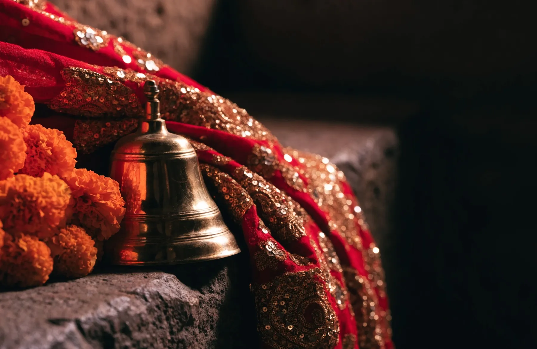 A red and gold chunni draped beside marigold flowers and a brass temple bell
