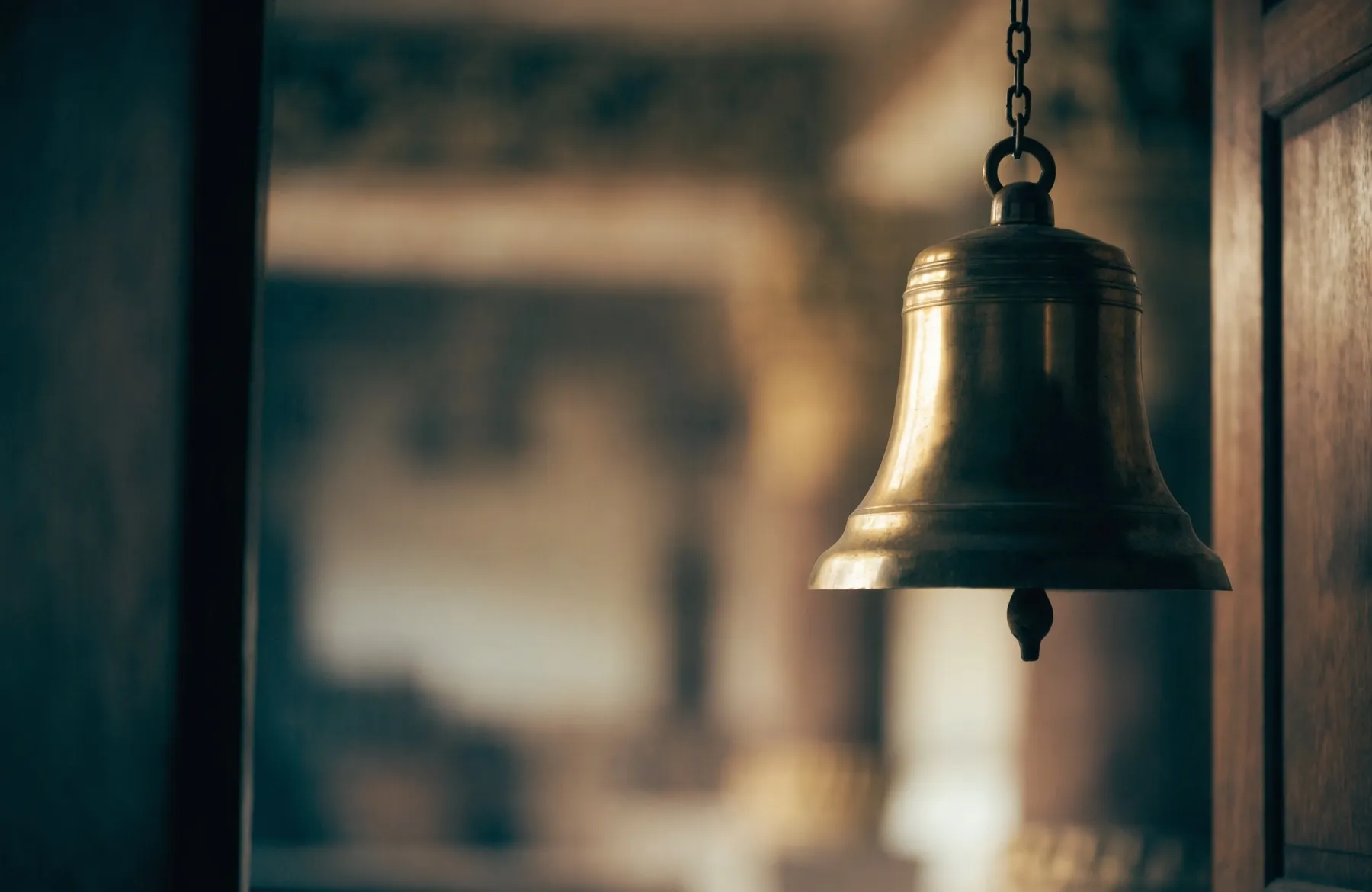 A polished brass temple bell hanging in a doorway, warm light glowing behind it
