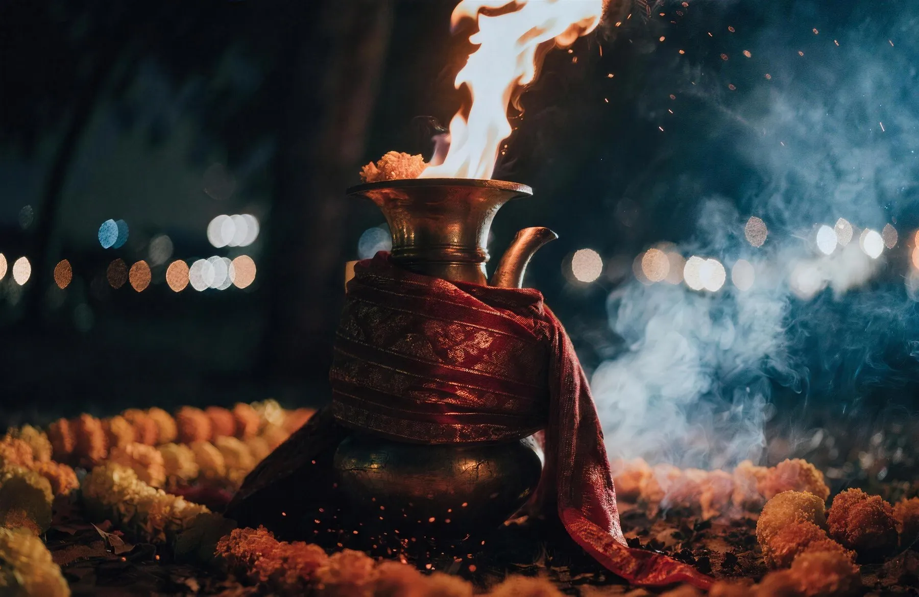 The jyoti burning in a brass vessel dressed in red and gold chunri, marigold garlands at its base