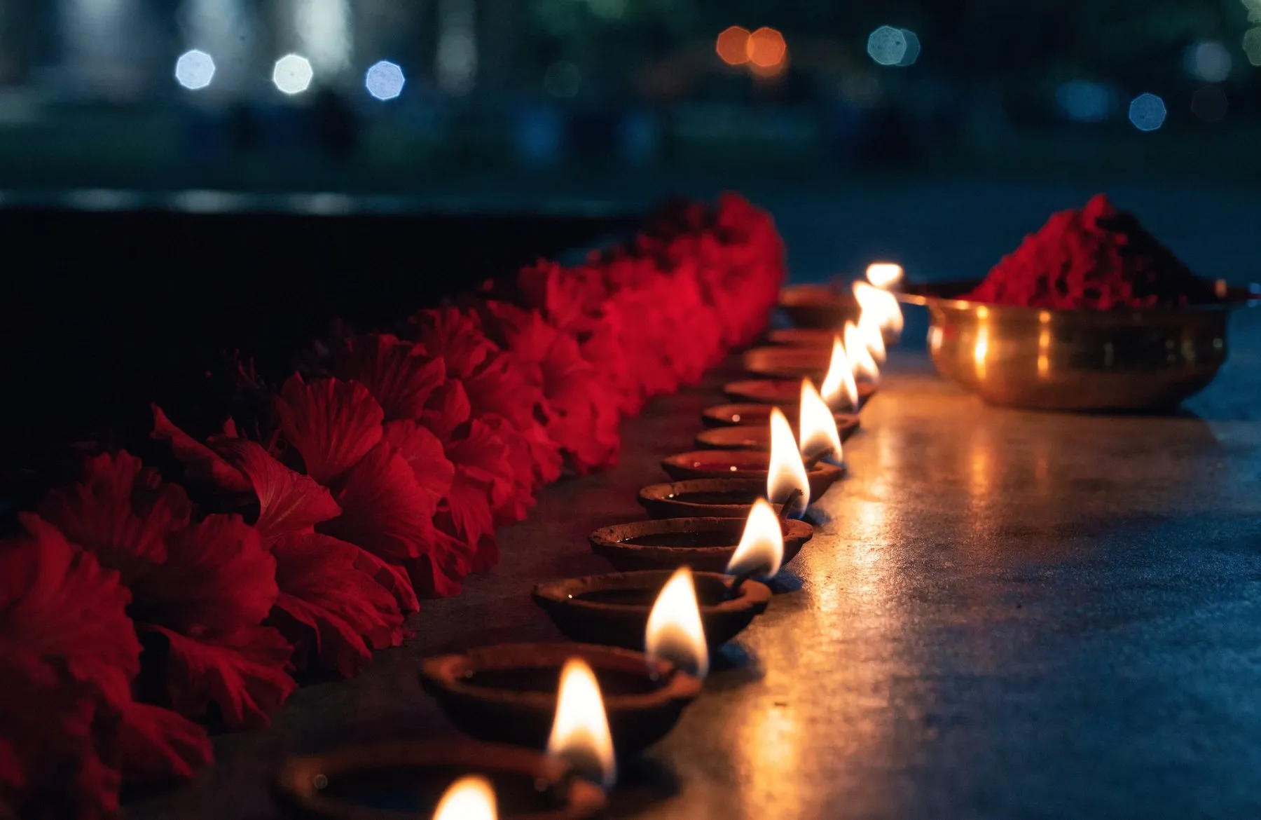 A garland of deep red hibiscus beside a row of clay diya lamps burning at night
