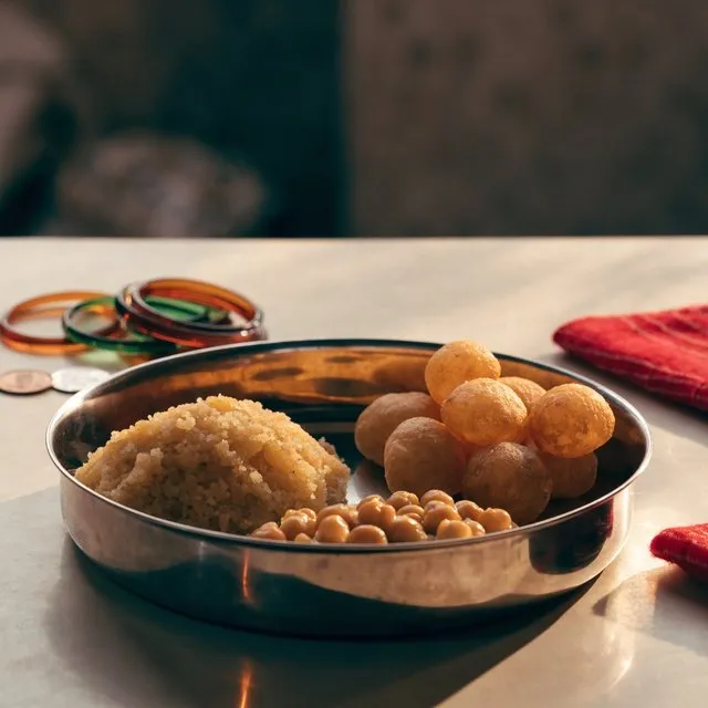A steel thali of halwa, puri and chana with bangles beside it