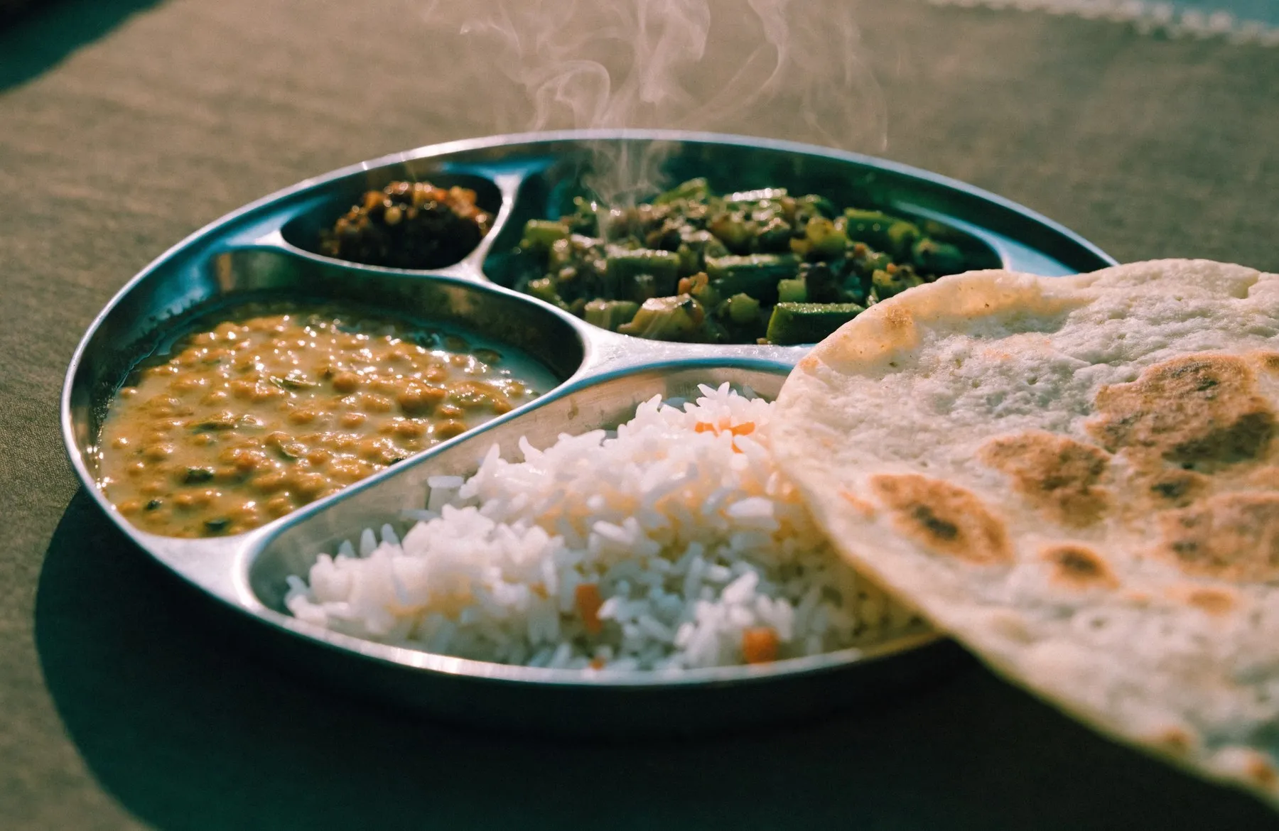 A steel thali served with dal, a vegetable sabzi, rice and a fresh roti