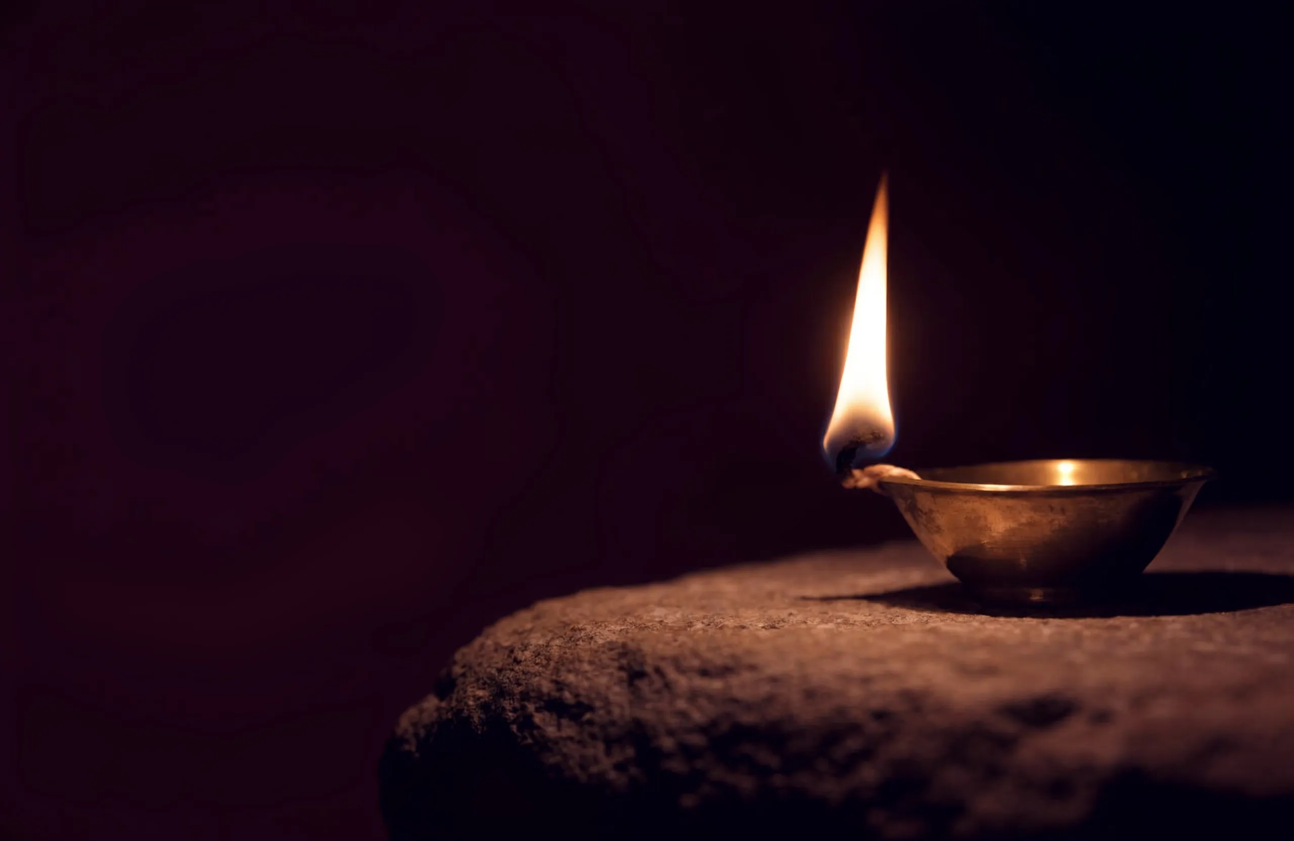 A brass diya burning with a single golden flame in the darkness