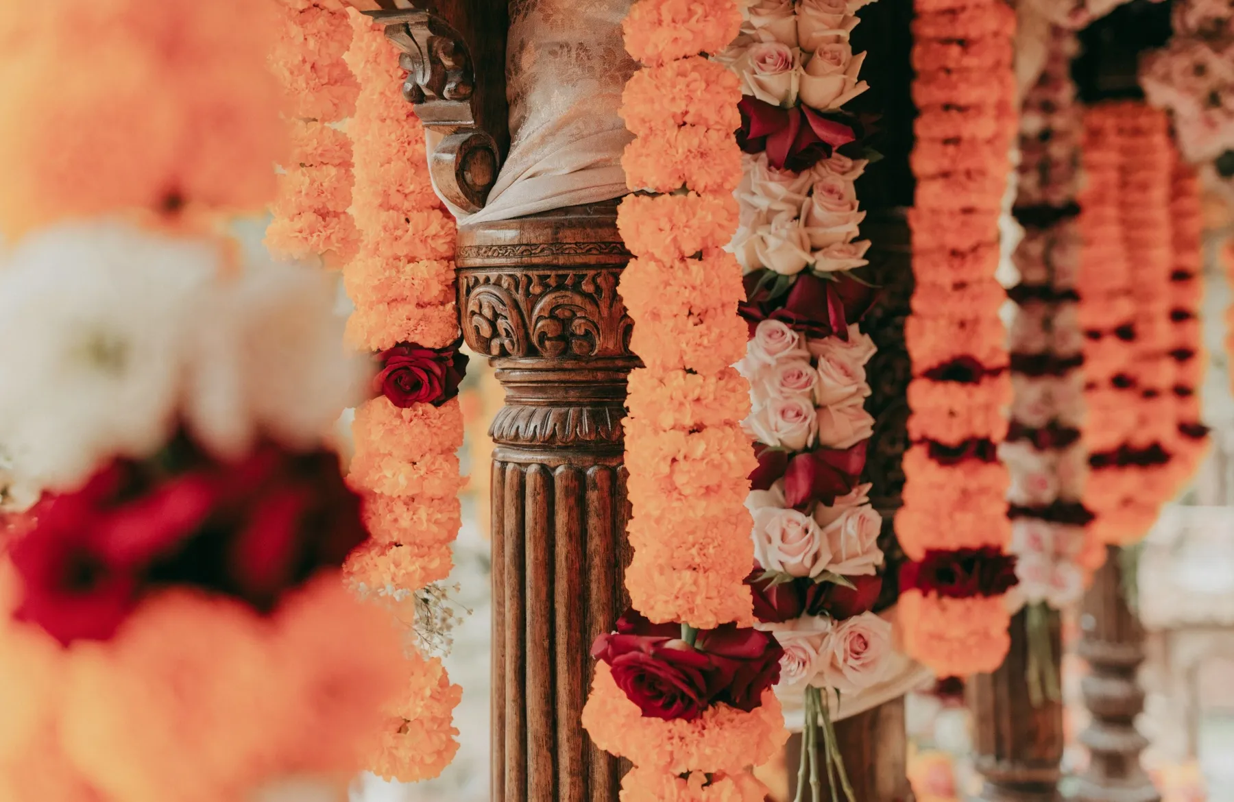 Marigold and rose garlands hanging in rich floral decoration around a carved canopy post