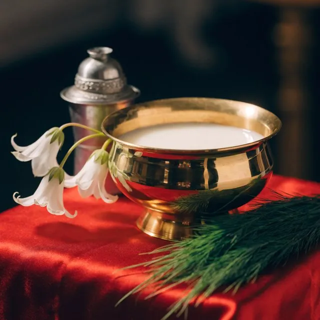 A brass bowl of milk with white flowers and durva grass on red silk