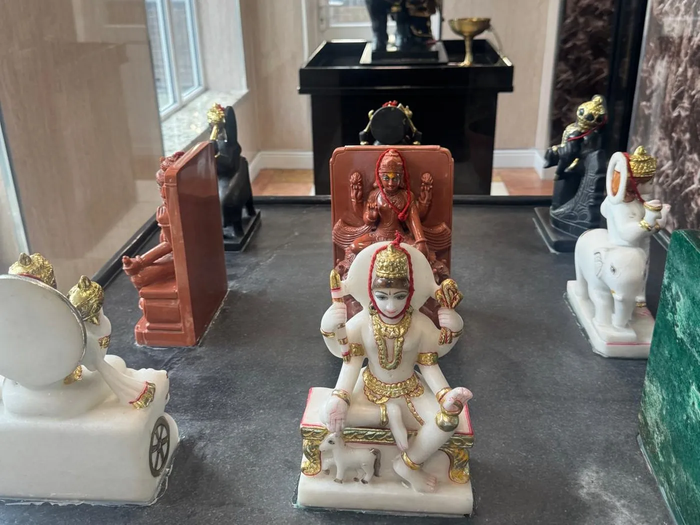The Navagraha murtis set out across their black plinth in the mandir, with the base of Shani Dev's shrine and a brass lamp on the ledge behind them
