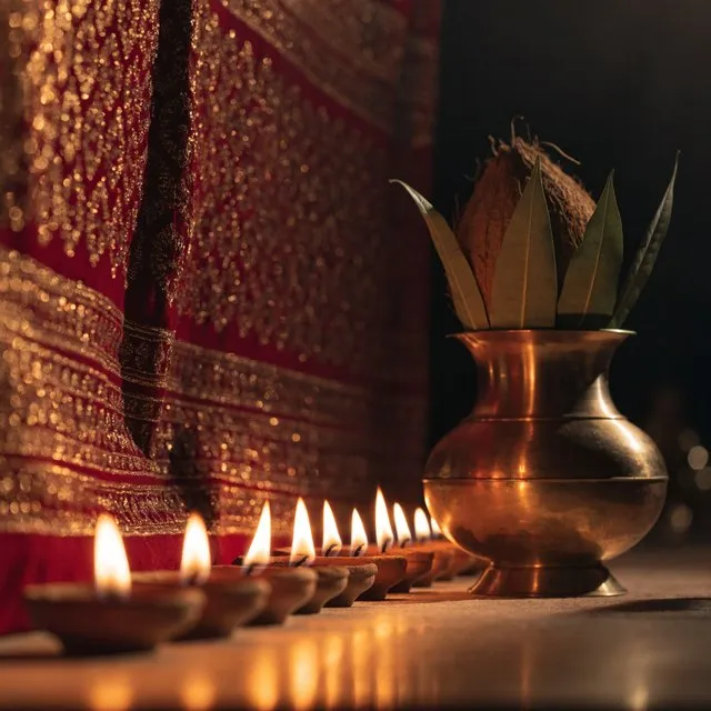 A row of nine diya lamps burning beside a brass kalash before a red chunri