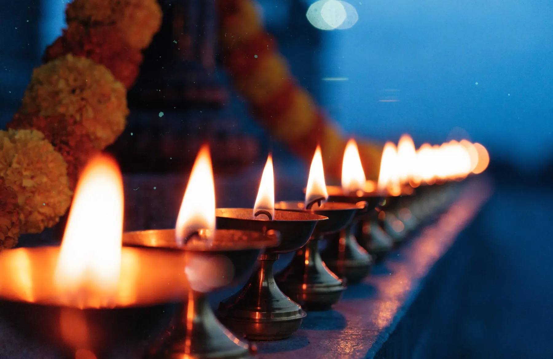 A row of small brass oil lamps burning along a ledge at dusk against a deep blue twilight sky