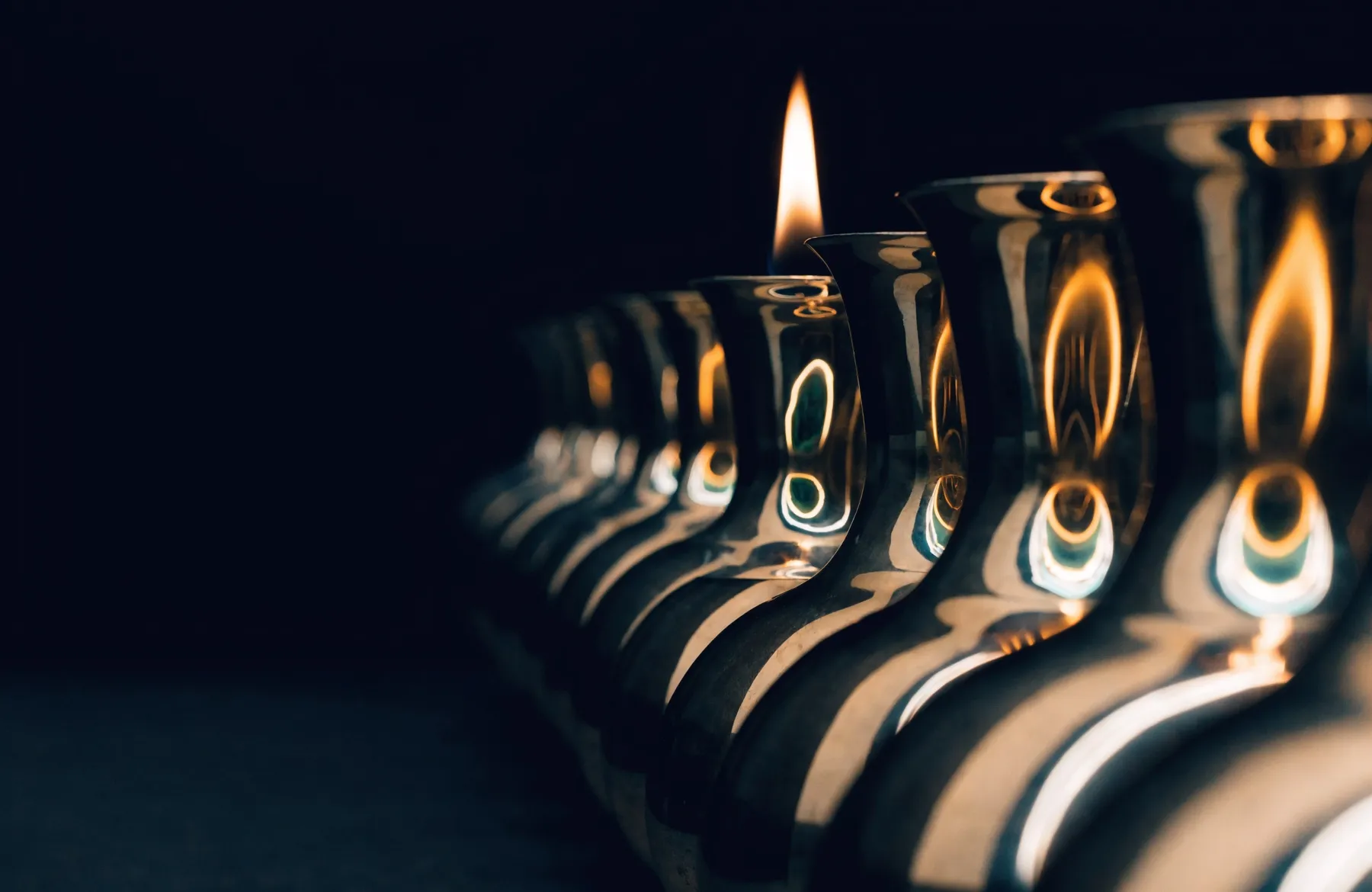 A single flame reflected many times over in a row of polished brass vessels — one light, many forms
