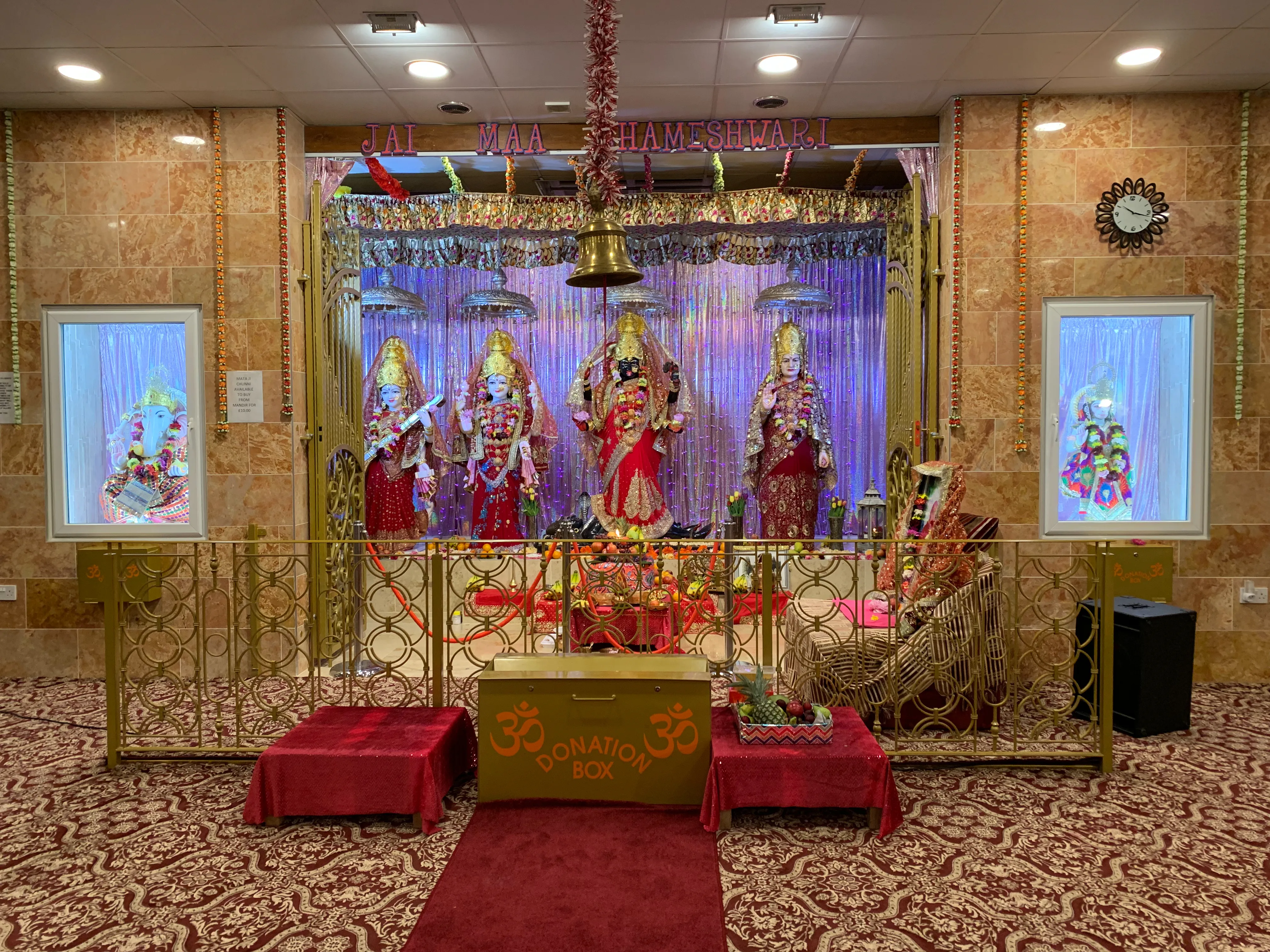 The prayer hall of Shri Maha Kali Bhameshwari Mandir — the main altar with murtis beneath silver chhatras, golden railings and red carpet