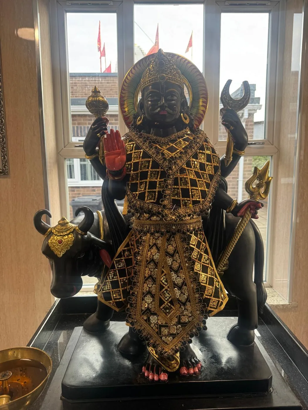 The murti of Shani Dev — dark-complexioned and four-armed, crowned, with a mace and trishul and his buffalo beside him