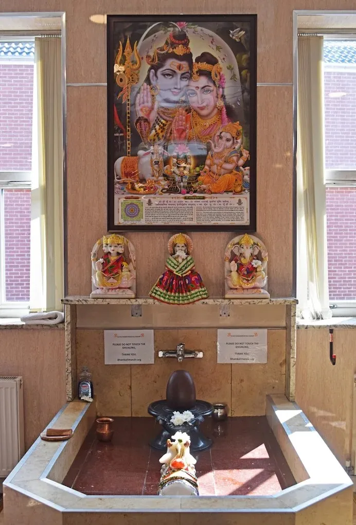 The Shivling shrine at the mandir — a black stone Shivling in a marble abhishek basin with Nandi before it, murtis of Shiv Ji, Maa Parvati and Ganesh above, and a framed Shiv Parivar picture behind