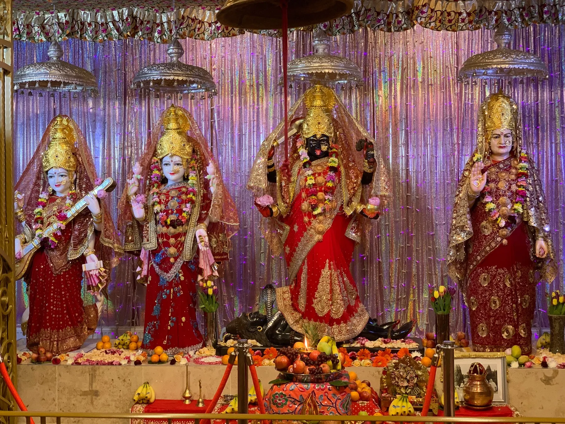 The altar before a shimmering purple bead curtain, all four Devis dressed in crimson and gold