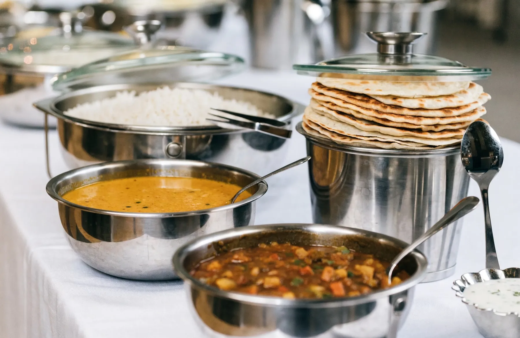 A vegetarian meal laid out in steel serving dishes — dal, sabzi, rice and a stack of fresh rotis