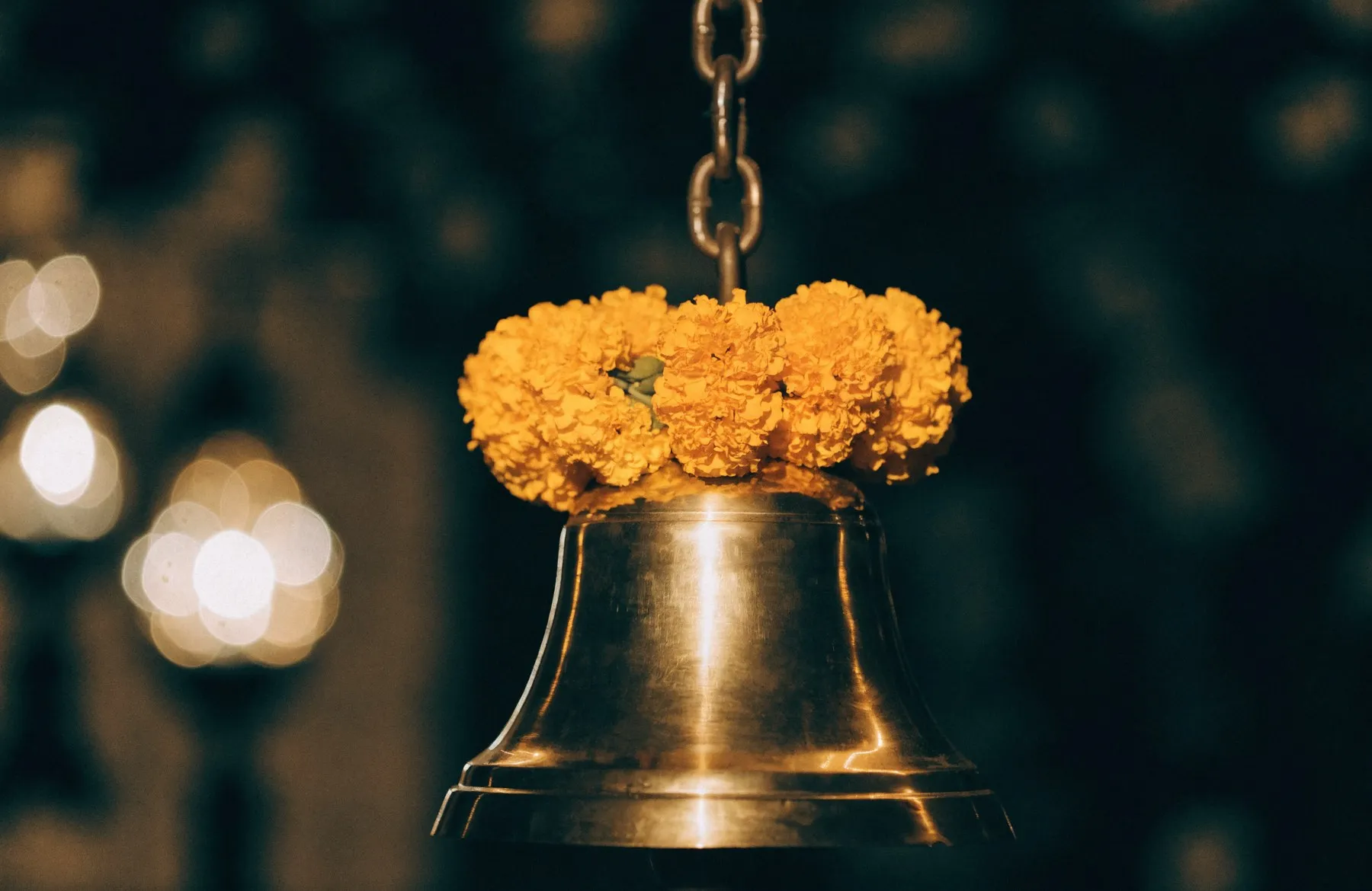 A brass temple bell hung with a marigold garland, glowing in warm lamplight