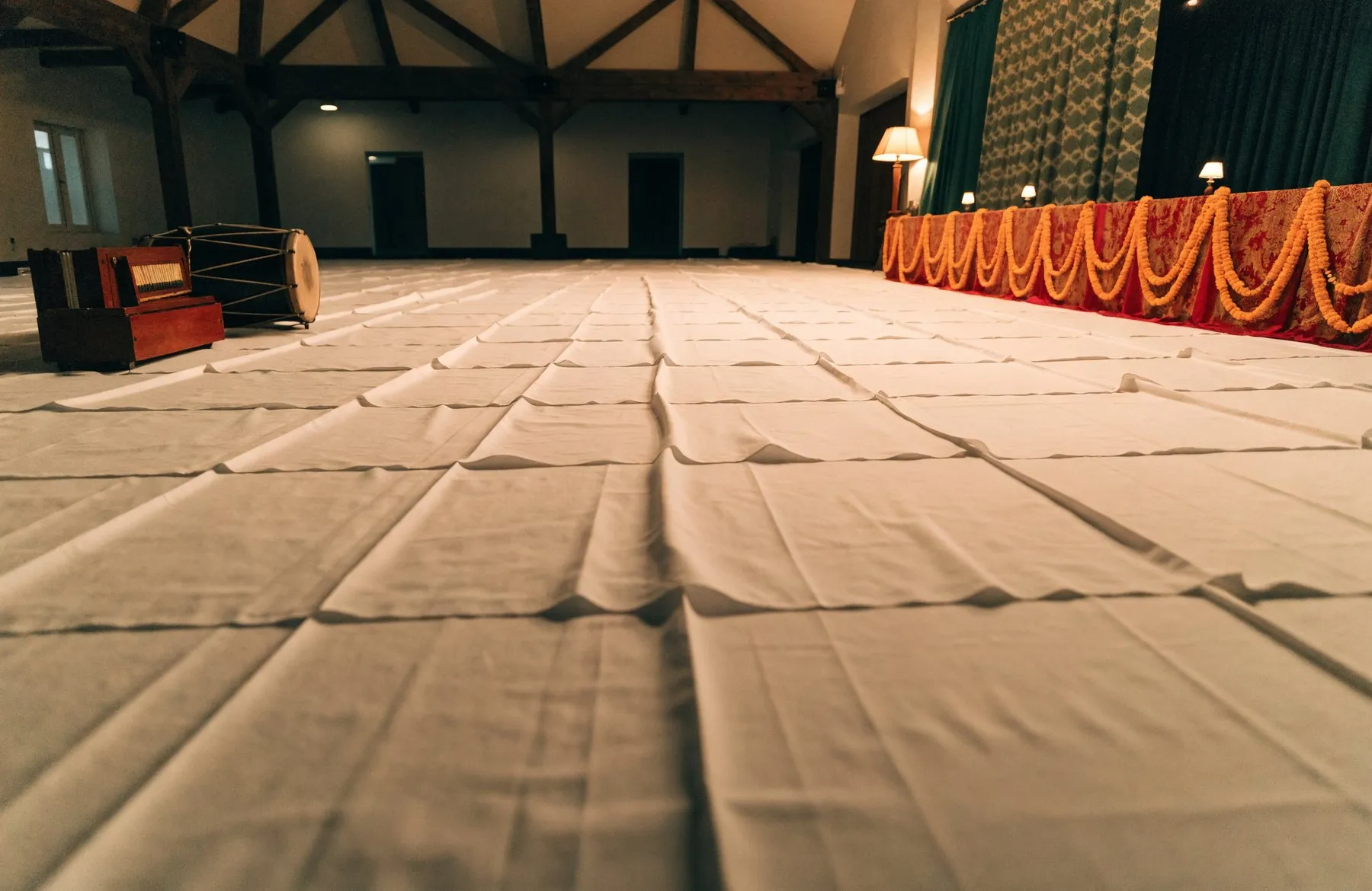 White cotton sheets spread across a hall floor with a harmonium and dholak set at the front