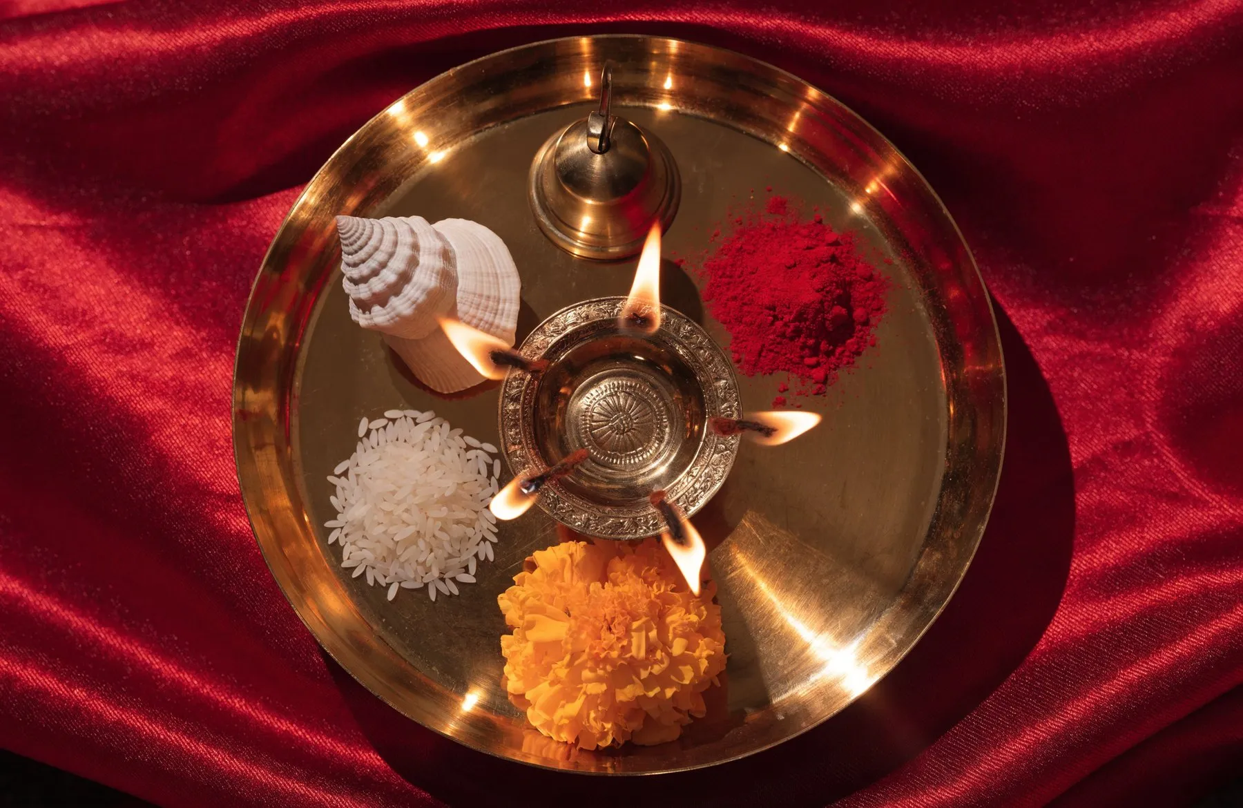 An aarti thali seen from directly above — a lit five-wick lamp at the centre with a conch, bell, kumkum and rice around it