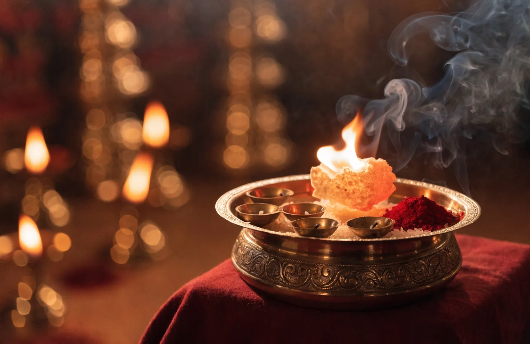 A brass aarti thali with a burning camphor flame and small wick lamps, smoke curling upward