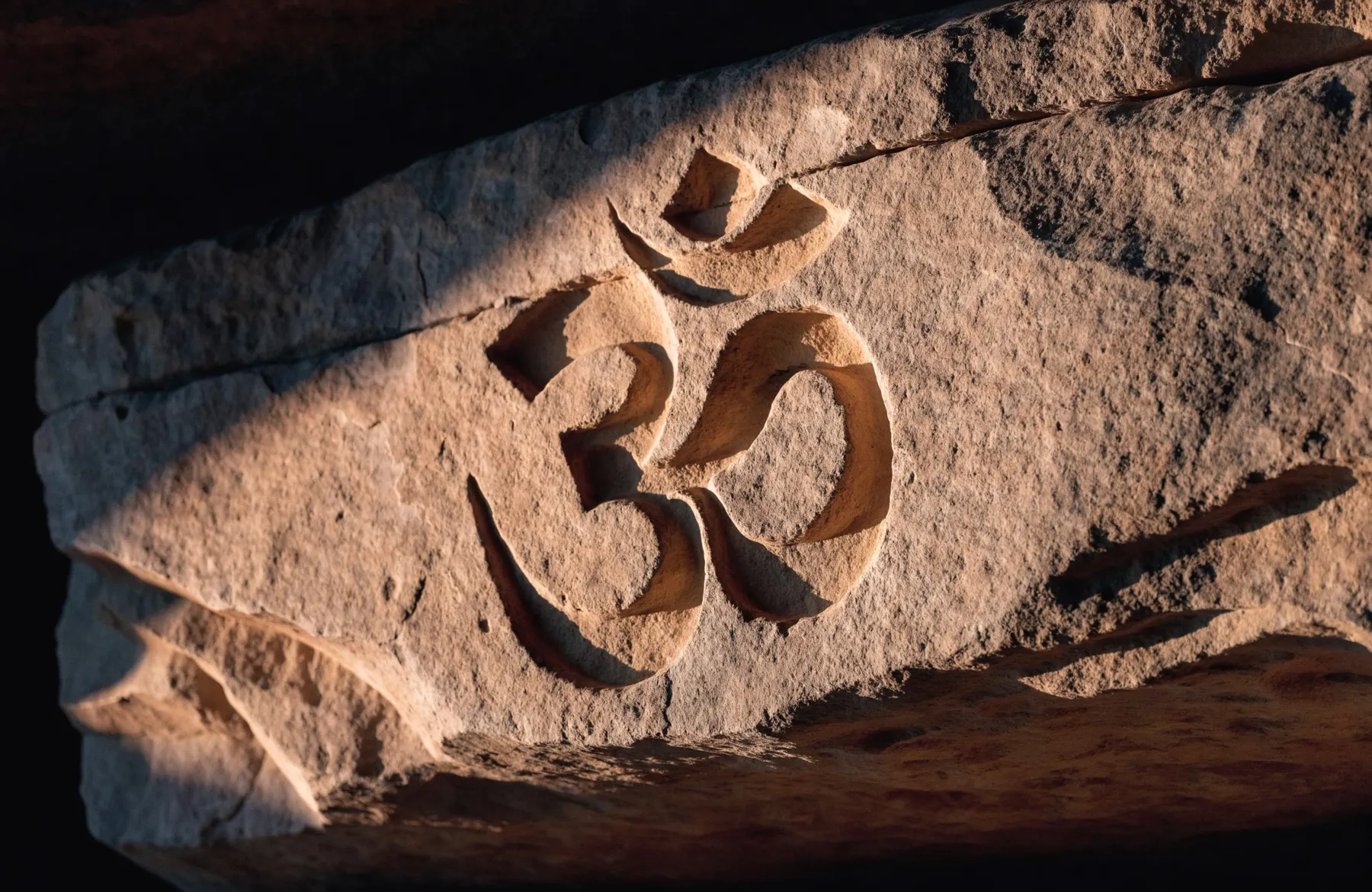 An ancient Om symbol carved into weathered sandstone, picked out by raking sunlight