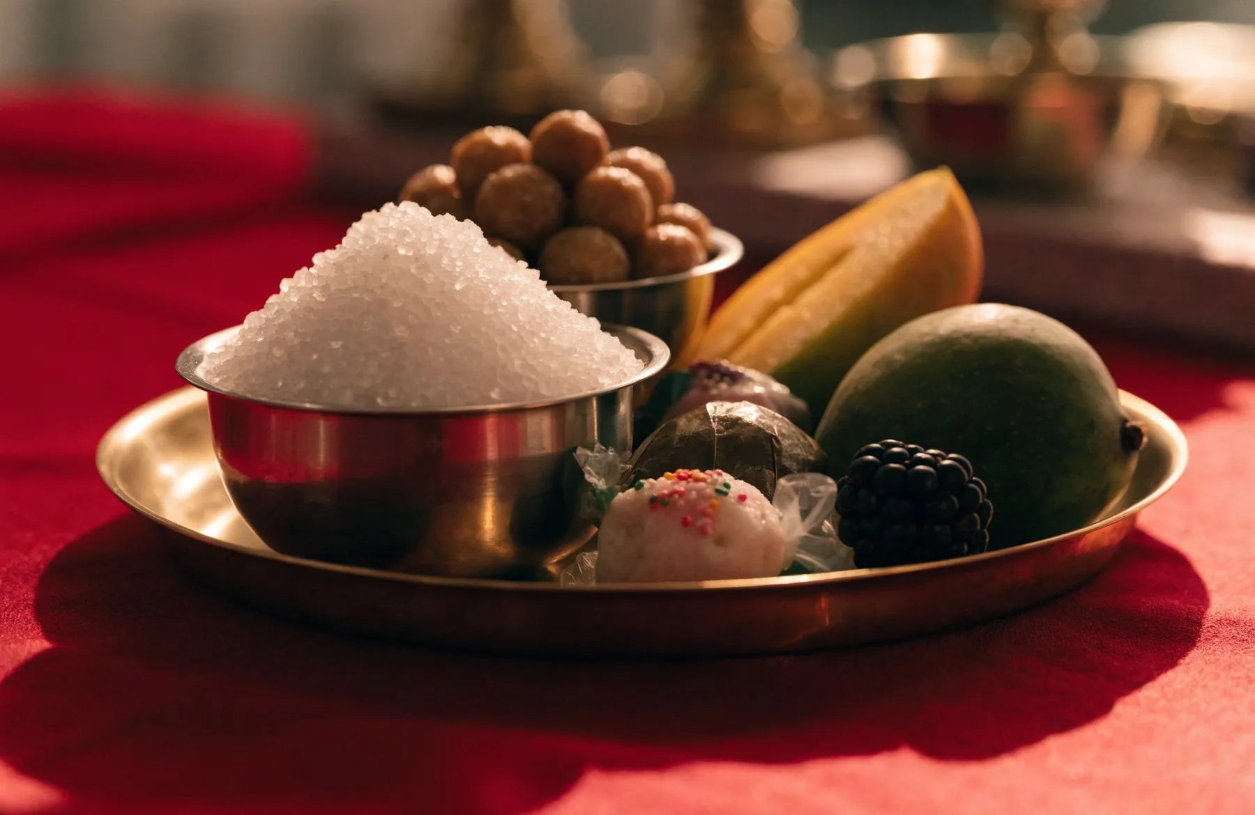 Steel bowls of sugar crystals, batasha sweets and fresh fruit set on a brass thali