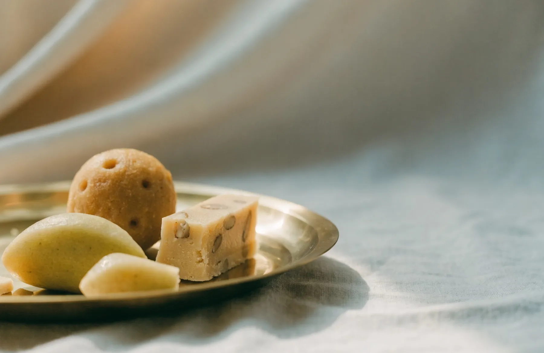 Laddoo, barfi and fresh fruit arranged on a brass plate on ivory cloth