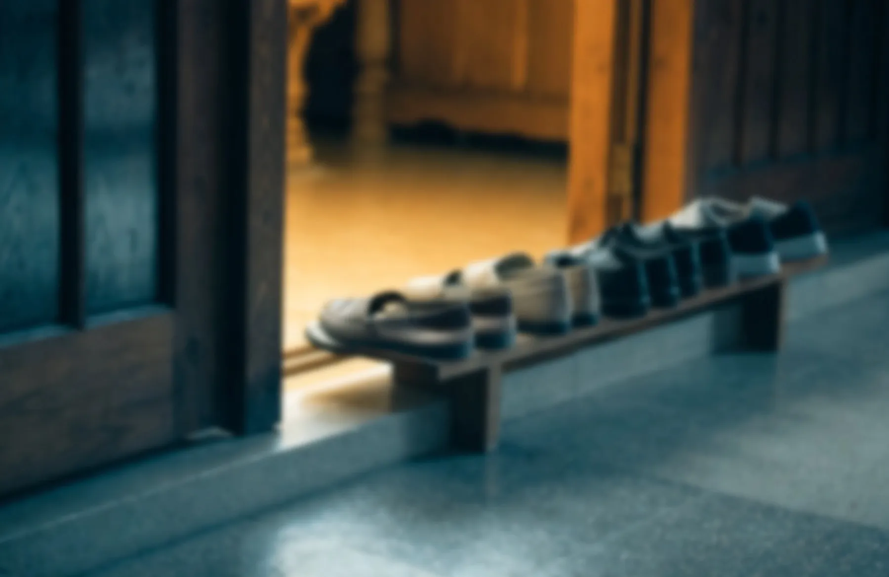 Shoes neatly removed and lined up on a rack outside a temple doorway, warm light spilling from within