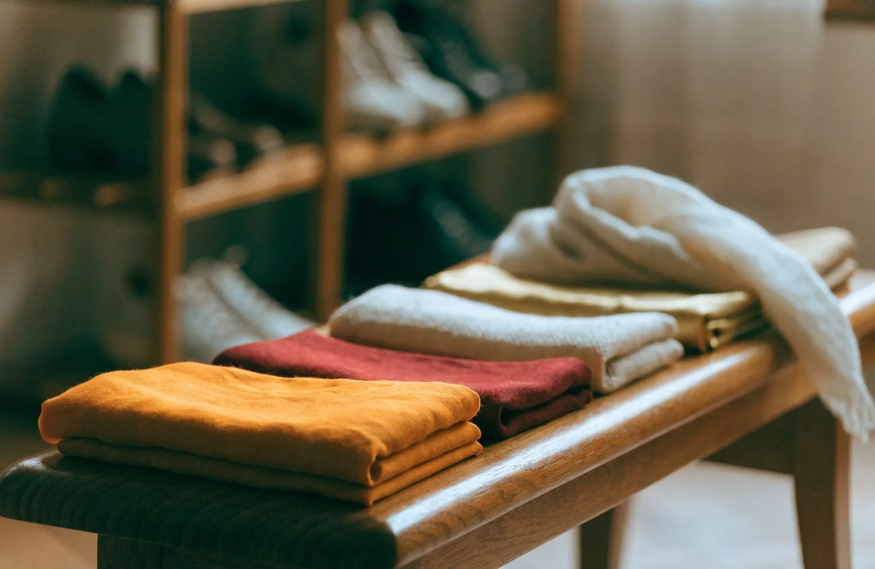 Folded shawls and scarves in saffron, deep red, cream and gold on a clean wooden bench